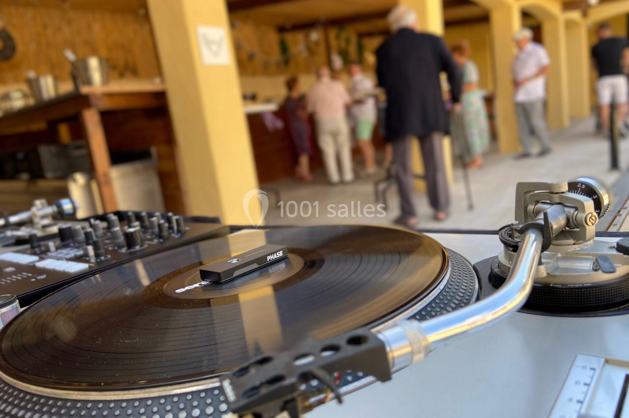Platine vinyle en gros plan avec un disque en lecture, en arrière-plan des personnes discutent dans un espace extérieur.