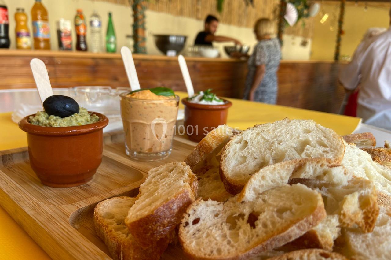 Assiette de tranches de pain accompagnées de trois tartinades dans des ramequins, posée sur une table en bois.