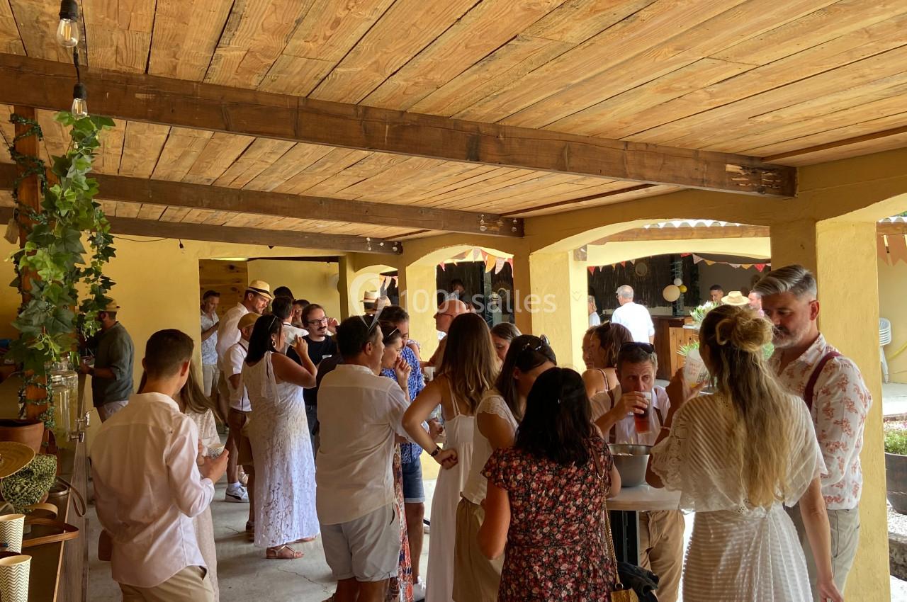 Des personnes discutent et partagent un moment convivial sous une terrasse en bois, décorée de plantes suspendues.