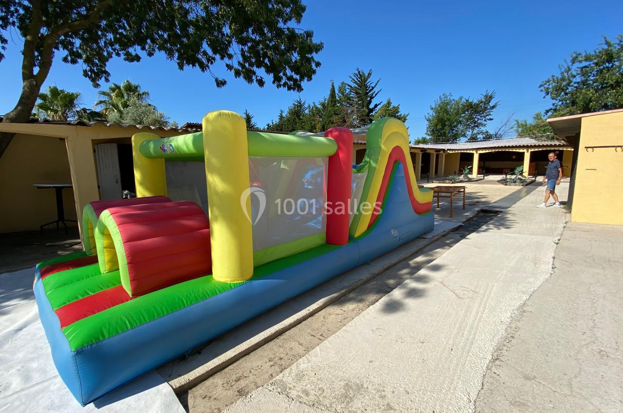 Structure gonflable colorée avec toboggan et tunnels, installée en extérieur sur une surface bétonnée.