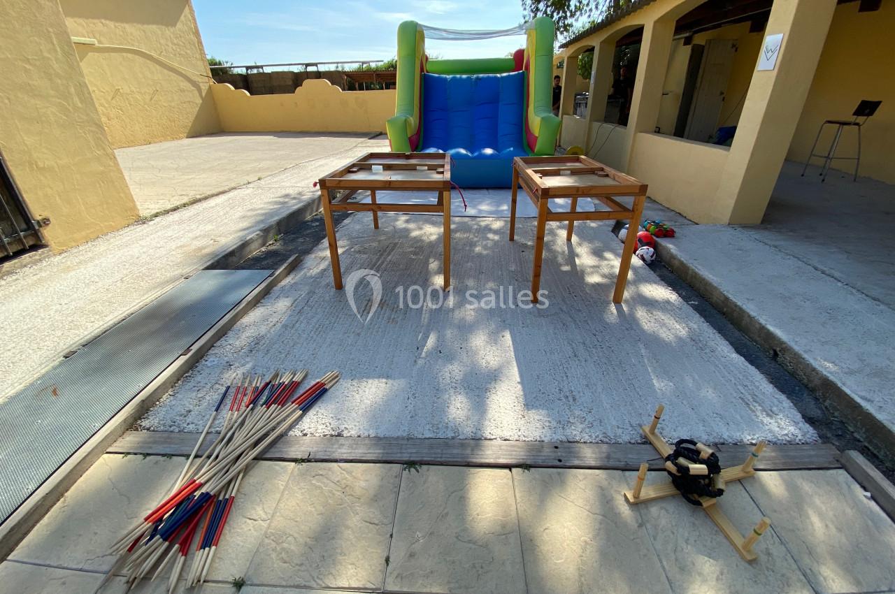 Deux tables en bois, un jeu de mikado géant, un jeu d'équilibre et une structure gonflable dans une cour extérieure.