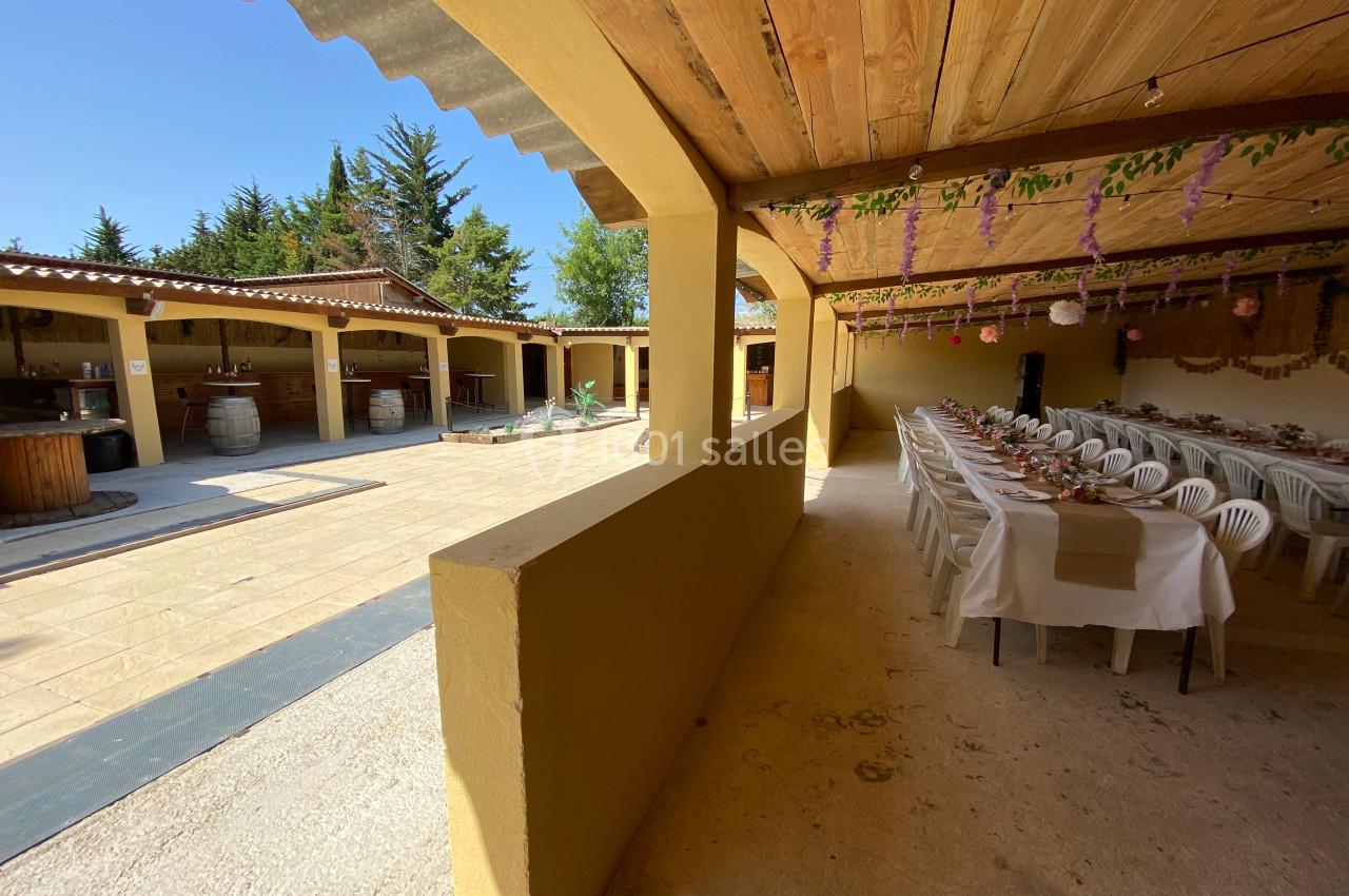 Espace extérieur couvert avec tables dressées pour un repas, décorations suspendues et vue sur une cour ensoleillée.