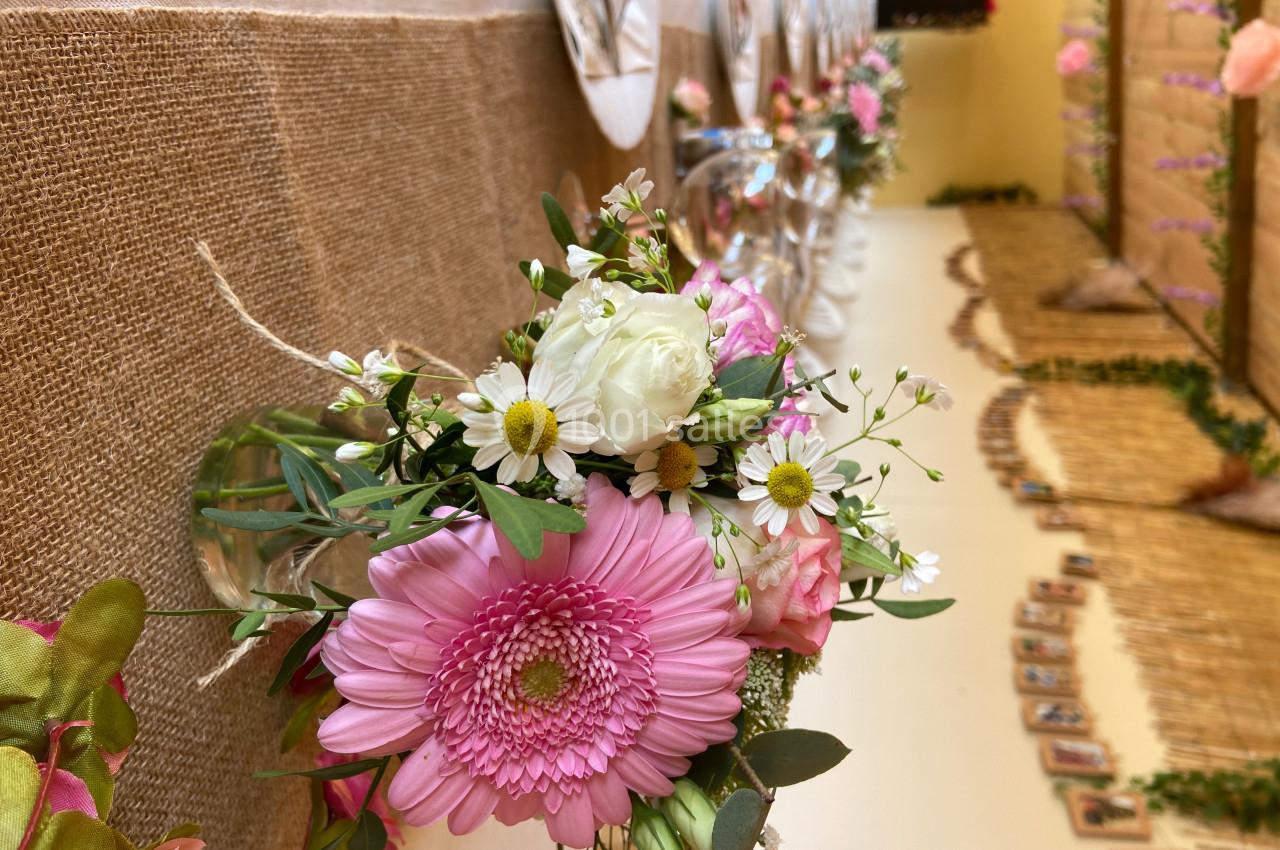 Bouquet de fleurs roses et blanches avec des marguerites, disposé sur une table recouverte de toile de jute.
