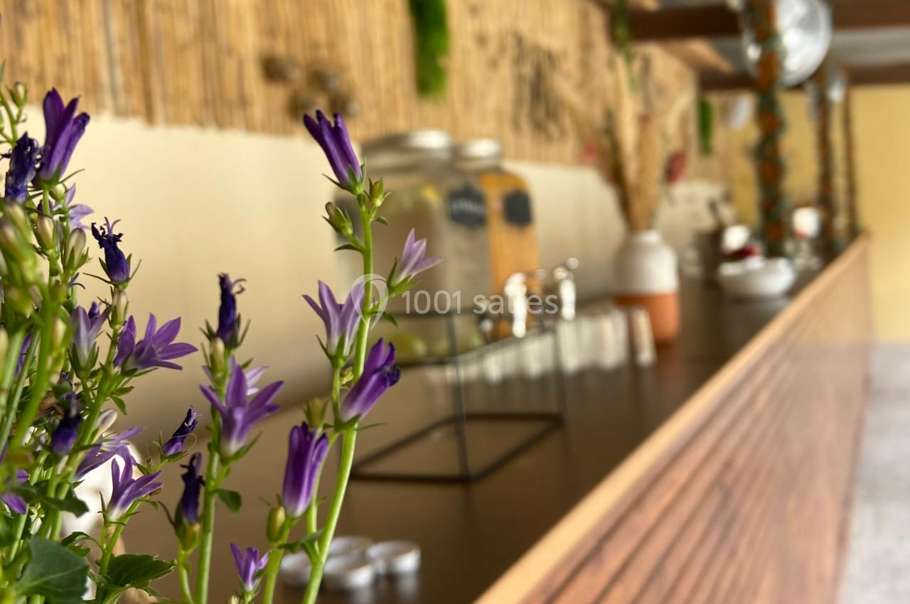Fleurs violettes au premier plan avec un comptoir en bois et une décoration naturelle en arrière-plan.