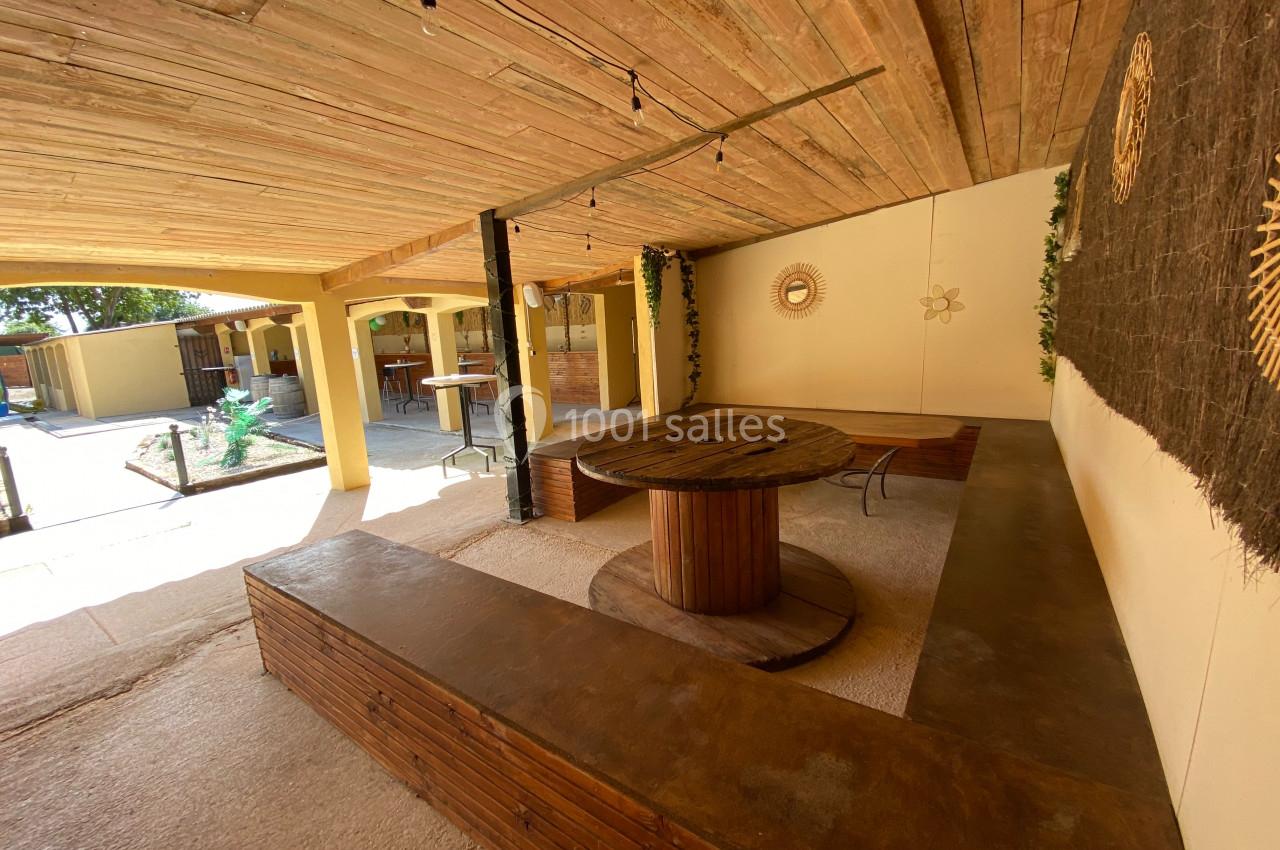 Espace extérieur couvert avec mobilier en bois, murs décorés et vue sur un jardin en arrière-plan.