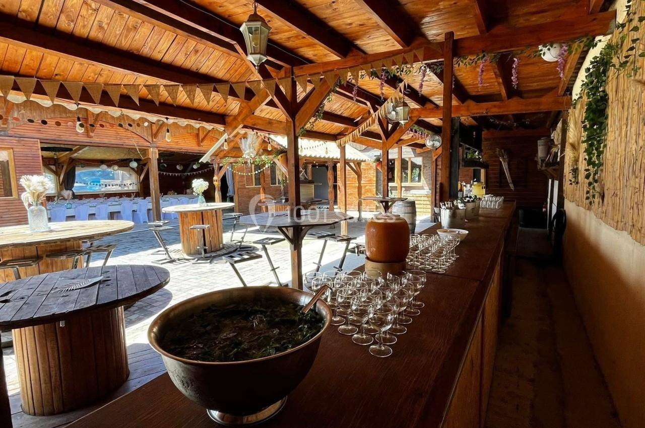 Salle en bois avec tables rondes, bar garni de verres et grand saladier, décorée pour un événement convivial.