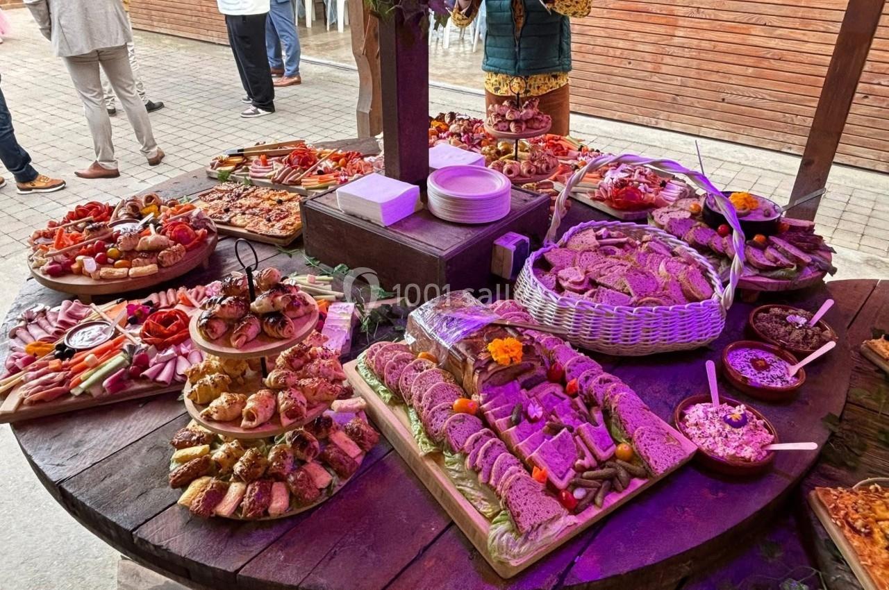 Table en bois garnie de divers plats, pains, charcuteries et amuse-bouches, présentés pour un buffet en extérieur.