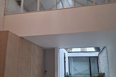 Façade d'une maison moderne en bois avec de grandes baies vitrées, entourée de murs en briques et végétation.