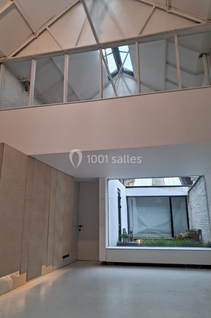 Intérieur lumineux avec plafond en verrière, murs blancs, et vue sur une petite cour végétalisée.