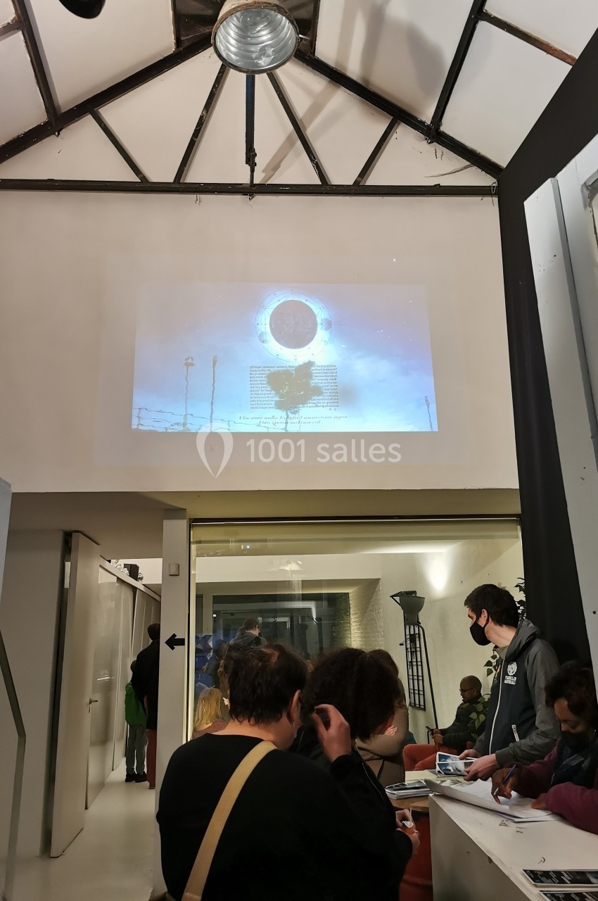 Projection d'une image sur un mur dans un espace intérieur avec des personnes assises et debout en arrière-plan.