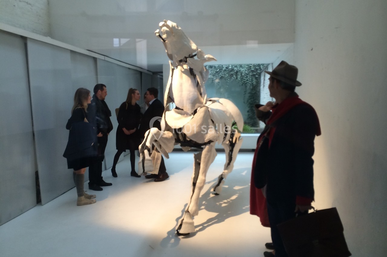 Un groupe de personnes observe une sculpture blanche de cheval dans un espace d'exposition moderne.