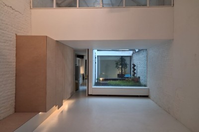 Façade d'une maison moderne en bois avec de grandes baies vitrées, entourée de murs en briques et végétation.