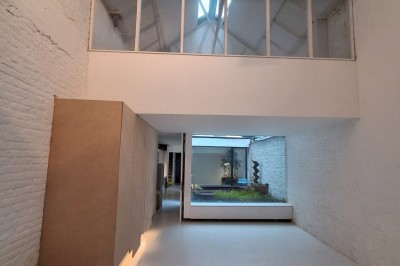 Façade d'une maison moderne en bois avec de grandes baies vitrées, entourée de murs en briques et végétation.