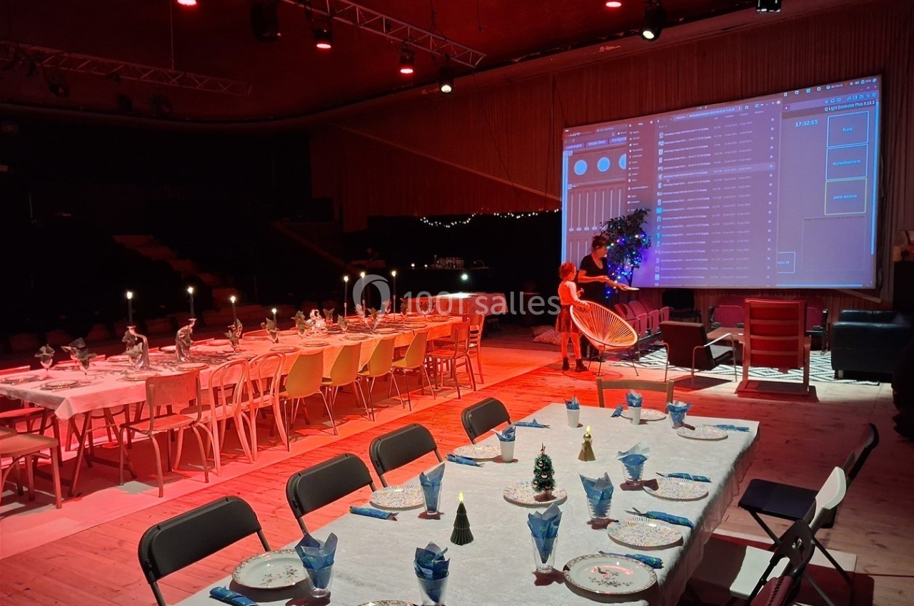 Salle décorée pour un événement, avec tables dressées, éclairage rouge et grand écran projetant une interface.