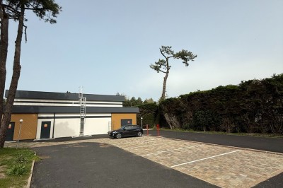 Parking vide avec quelques places pavées, une voiture stationnée, un bâtiment moderne et des arbres en arrière-plan.