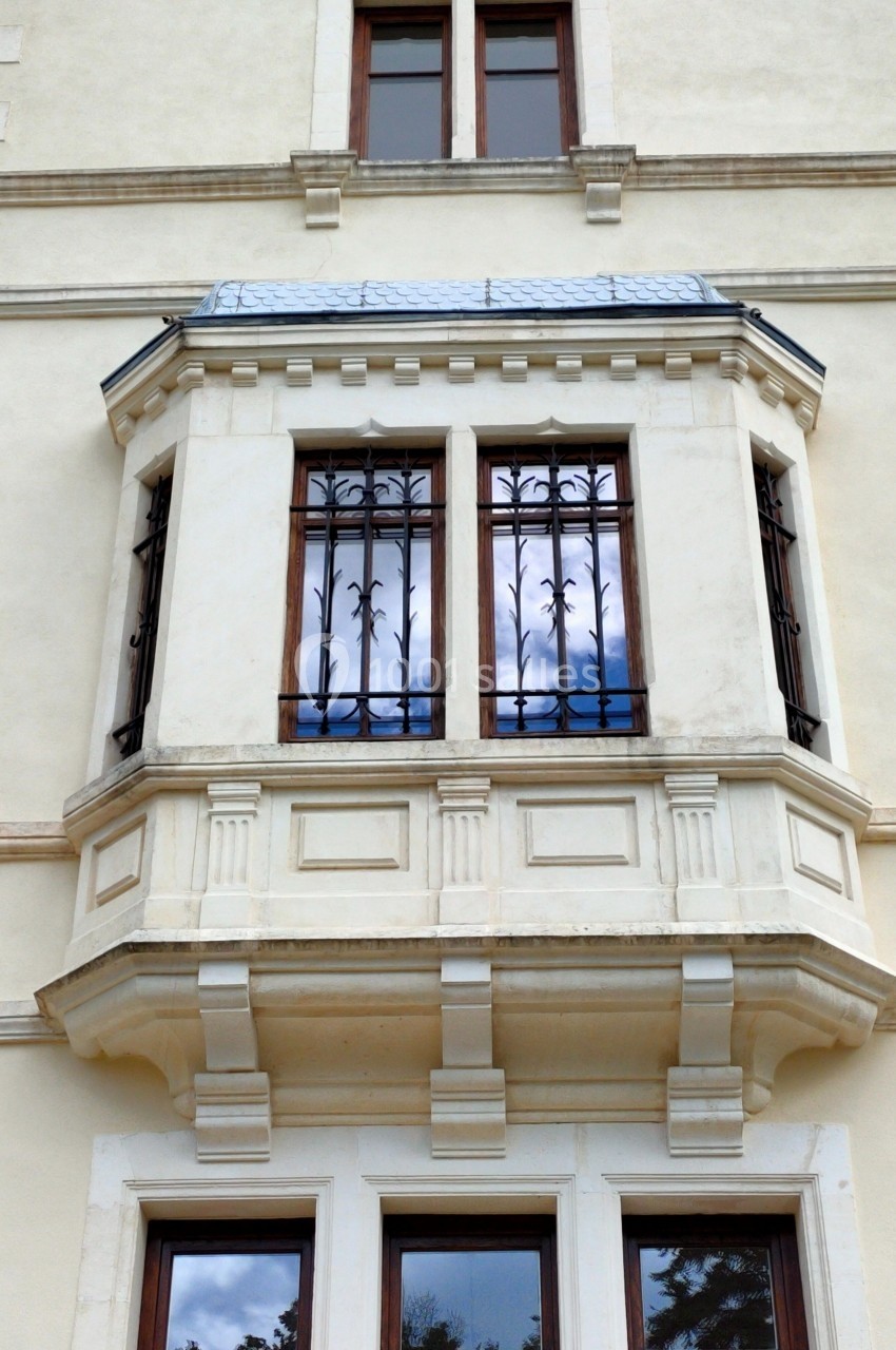 Façade d'un bâtiment avec une fenêtre en saillie ornée de grilles en fer forgé et un toit en ardoise.