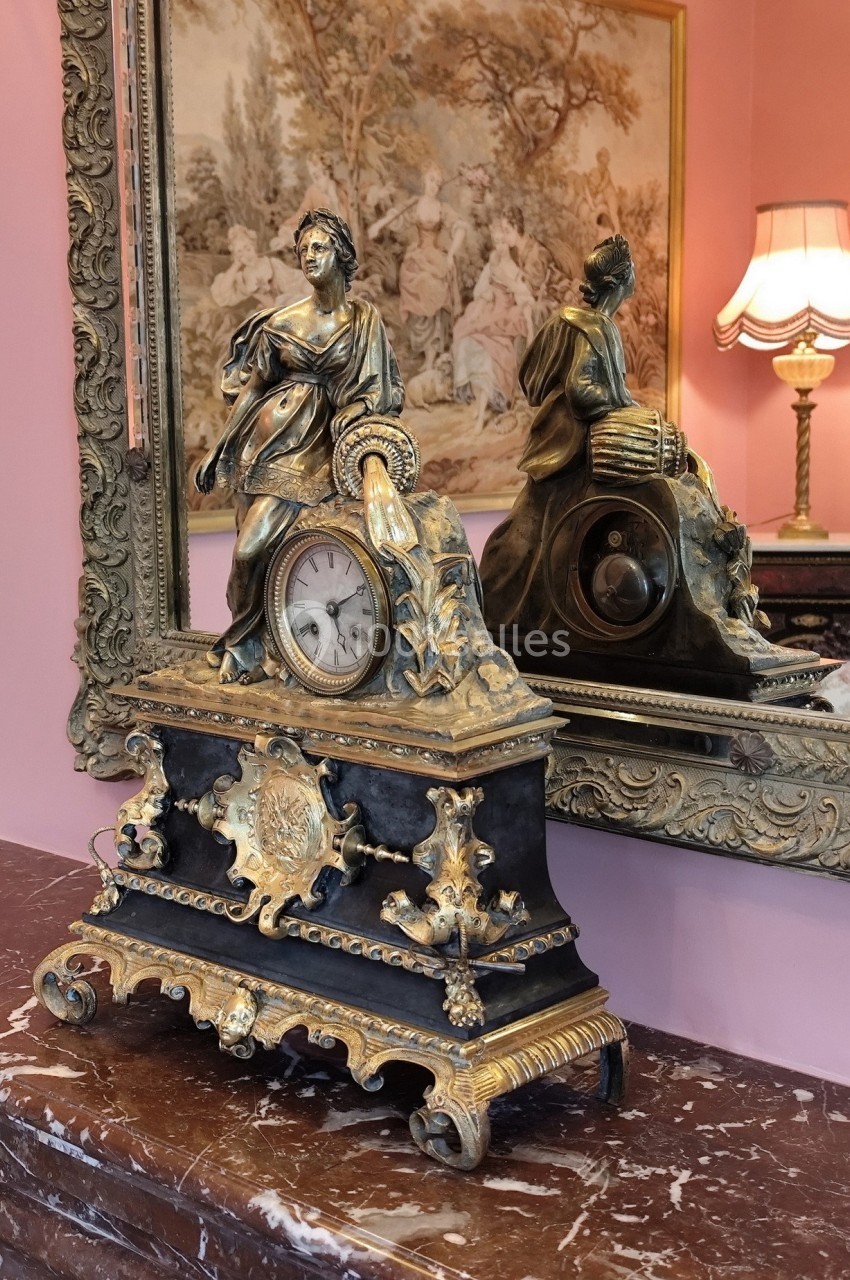 Horloge ancienne ornée de sculptures en bronze doré, posée sur un meuble en marbre devant un miroir décoratif.