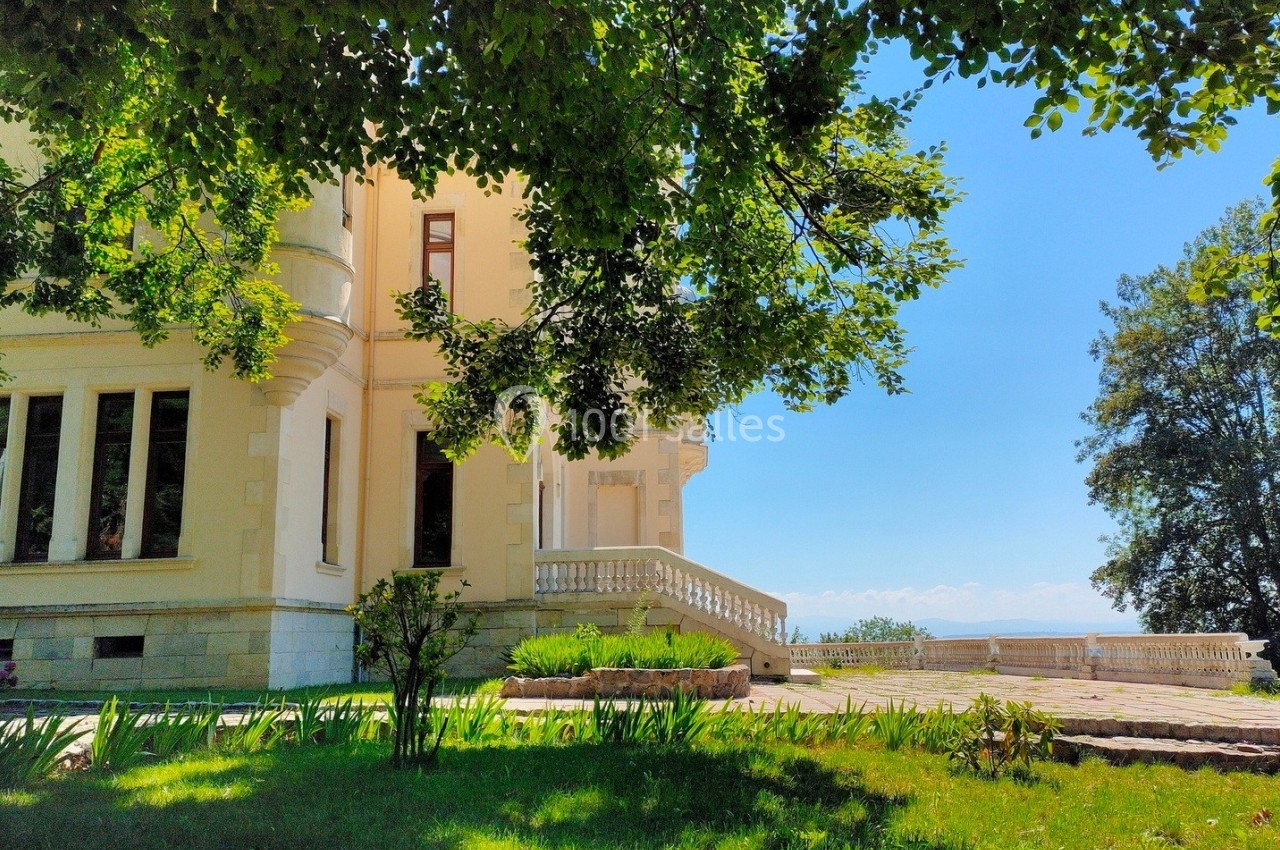Façade d'un bâtiment élégant entouré de verdure, avec une terrasse donnant sur un ciel dégagé.