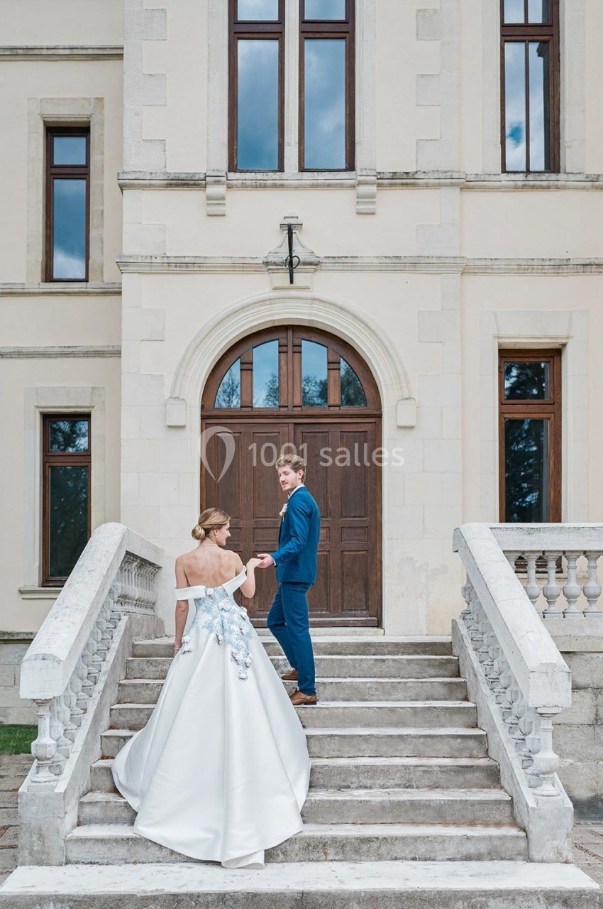 Un couple en tenue de mariage monte les marches d'un bâtiment ancien avec une grande porte en bois.
