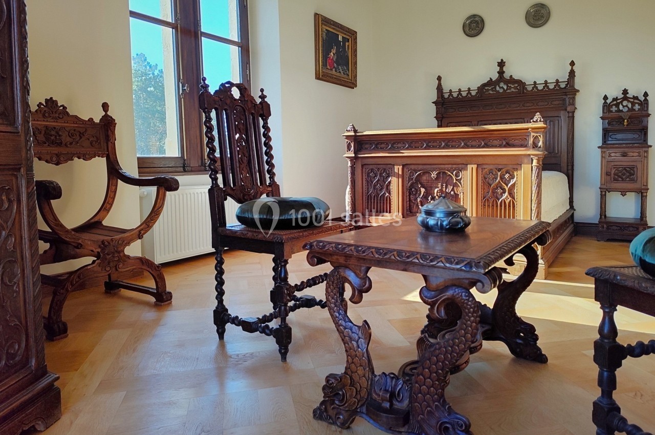 Mobilier en bois sculpté dans une chambre lumineuse avec lit, chaises et table ornés de détails décoratifs.