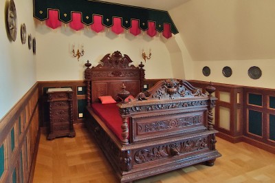 Miniature Chambre Héraldique Allée bordée de jeunes arbustes menant à une porte en fer, entourée d'arbres et d'un espace herbeux.