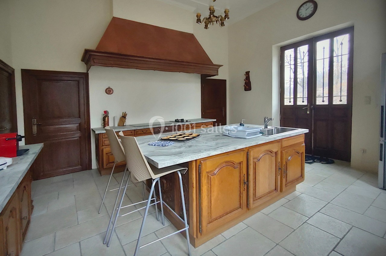 Cuisine spacieuse avec îlot central en bois, plan de travail en marbre, grande hotte et porte-fenêtre donnant sur l…