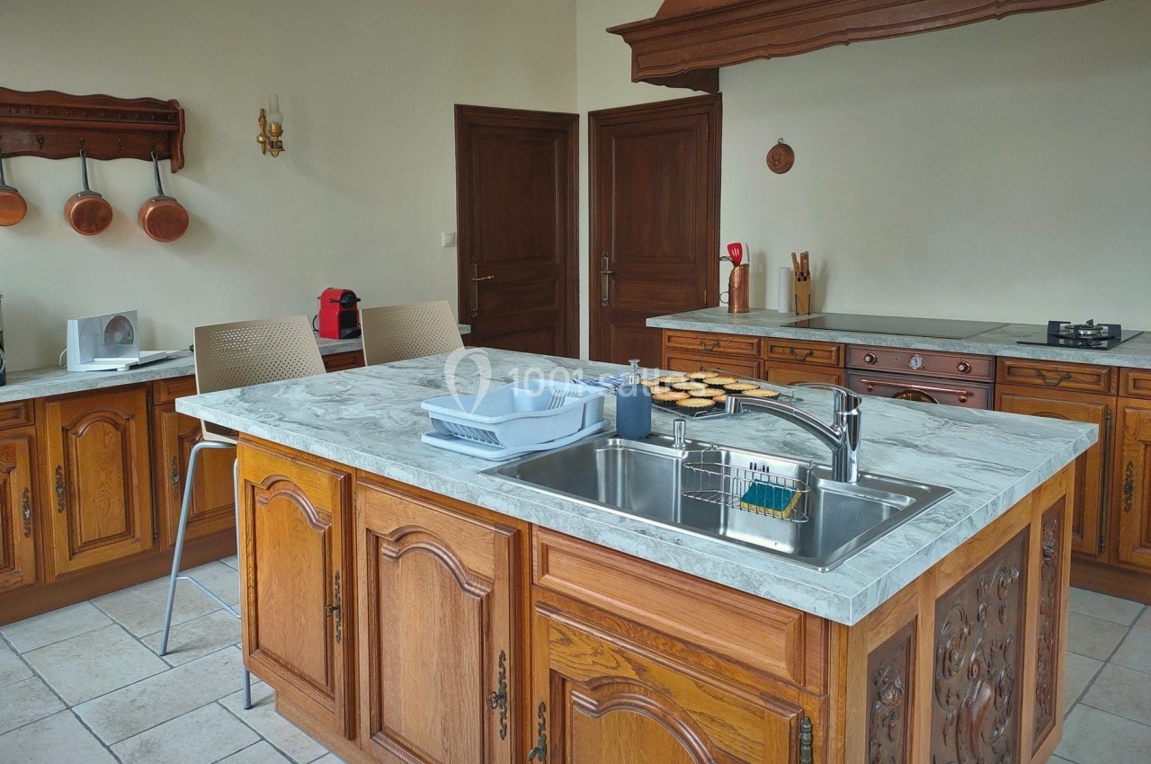 Cuisine traditionnelle avec meubles en bois sculpté, îlot central en marbre, évier intégré et ustensiles accrochés au mur.