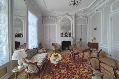 Miniature Grand Salon Allée bordée de jeunes arbustes menant à une porte en fer, entourée d'arbres et d'un espace herbeux.