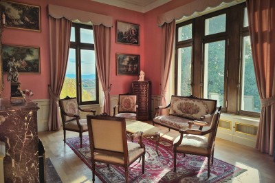 Miniature Petit Salon Allée bordée de jeunes arbustes menant à une porte en fer, entourée d'arbres et d'un espace herbeux.