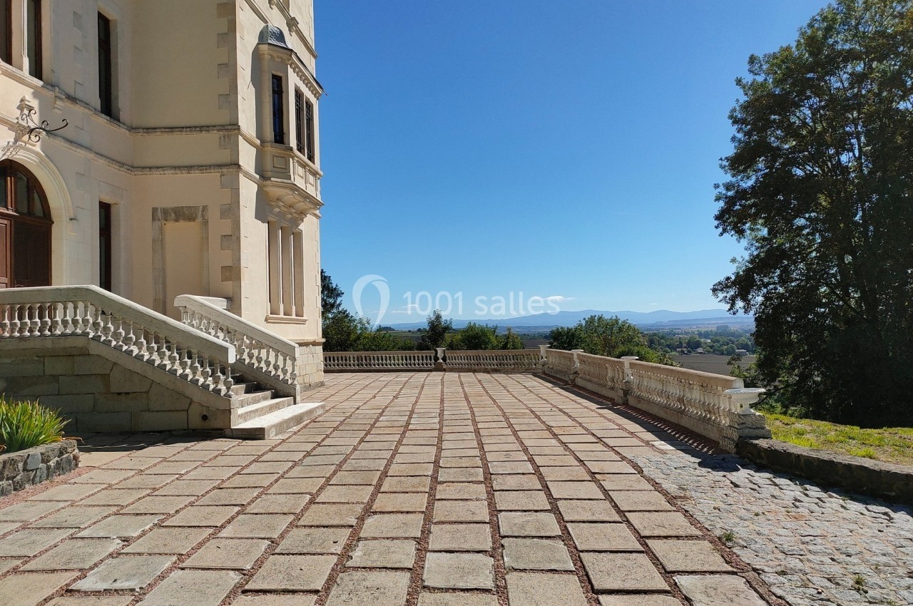 Terrasse pavée d'un bâtiment historique avec vue dégagée sur un paysage vallonné et un ciel bleu.