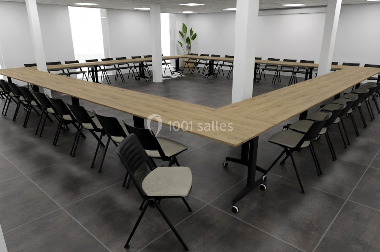Salle de réunion avec tables en U en bois clair et chaises noires sur un sol carrelé gris, éclairée par des plafonniers.