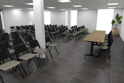 Salle de réception avec de longues tables dressées, chaises blanches et décoration sobre dans un espace lumineux.