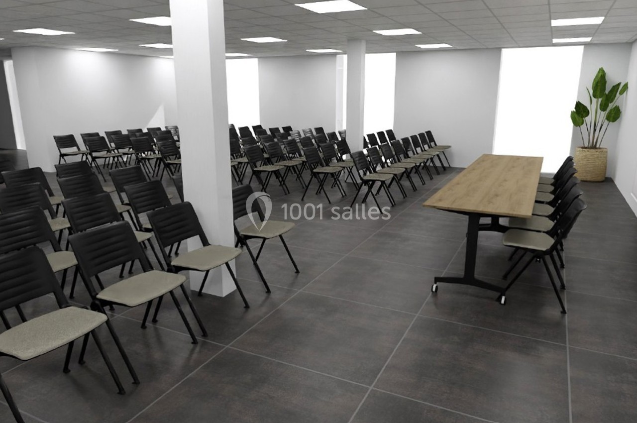 Salle de conférence avec rangées de chaises noires et une table en bois, éclairée par des lumières au plafond.