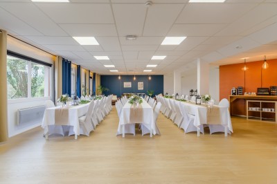Terrasse avec tables, chaises, parasols blancs et piscine adjacente, entourée de verdure.