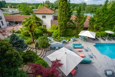 Terrasse avec tables, chaises, parasols blancs et piscine adjacente, entourée de verdure.