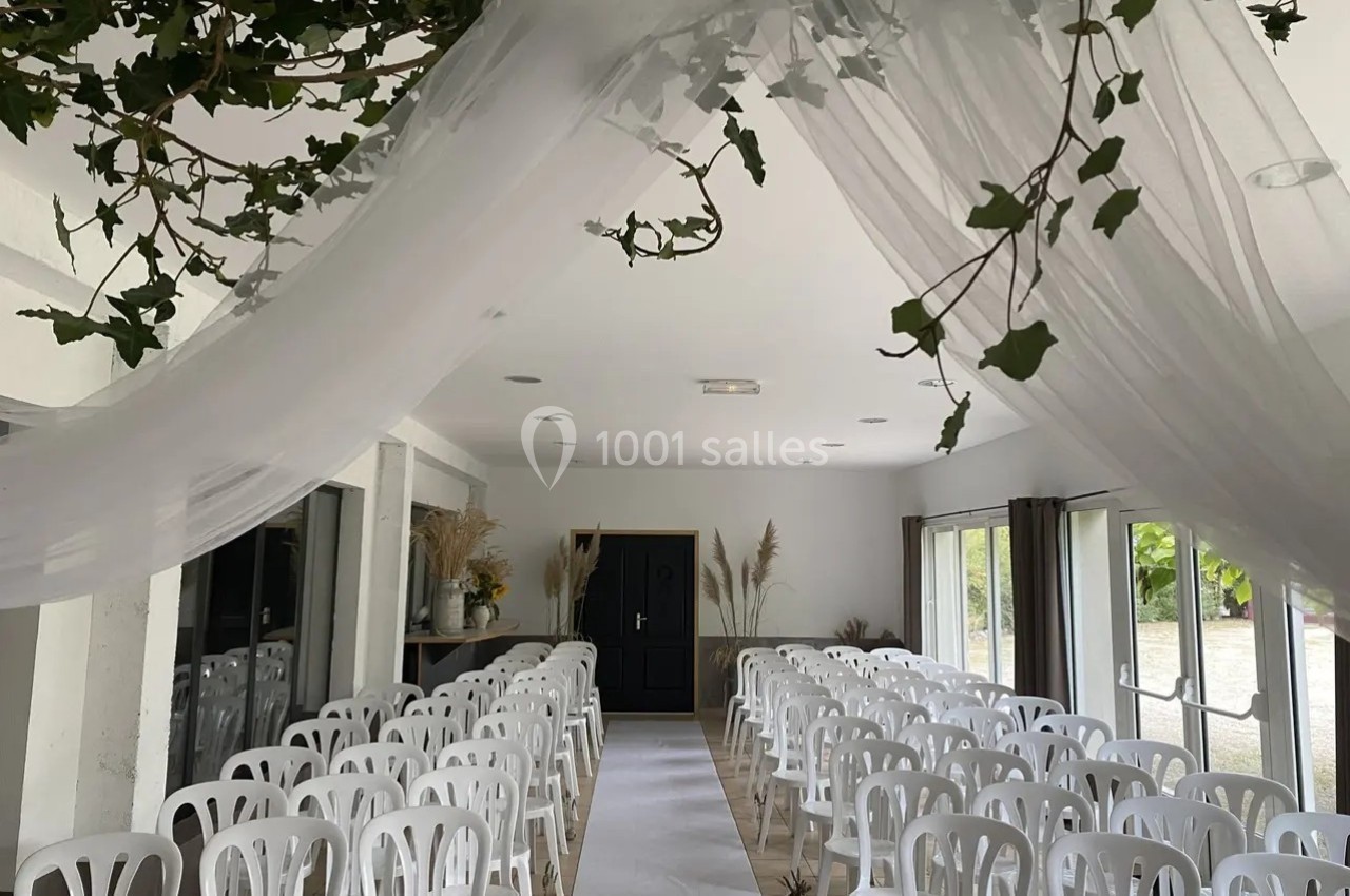 Salle de réception décorée avec des chaises blanches alignées, un voile suspendu et des branches de lierre.