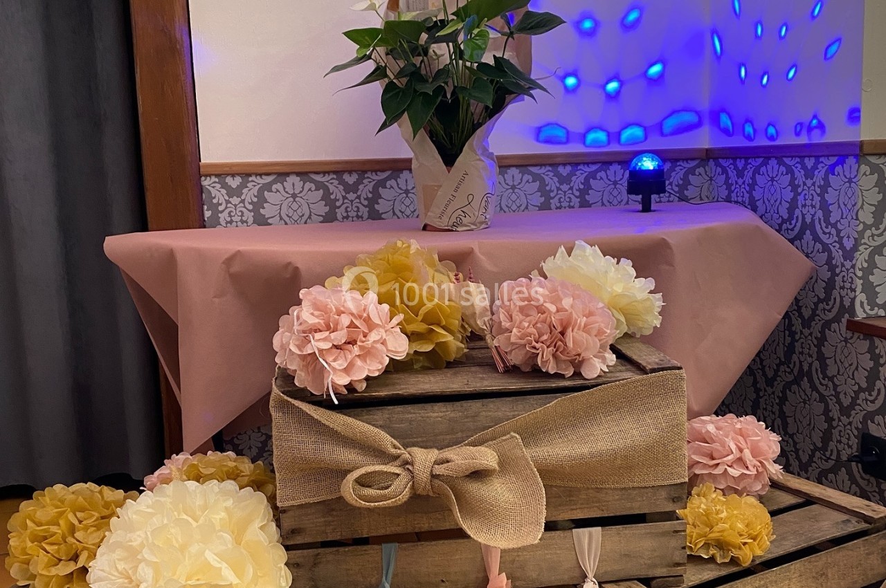 Décoration composée de caisses en bois ornées de fleurs en papier, avec une table et une plante en arrière-plan.