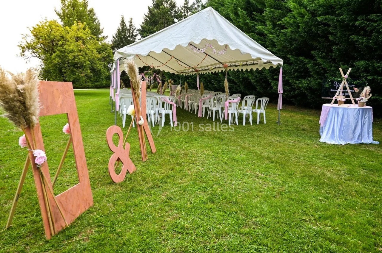 Tente blanche décorée pour un événement en extérieur, avec chaises alignées et ornements floraux sur une pelouse verte.