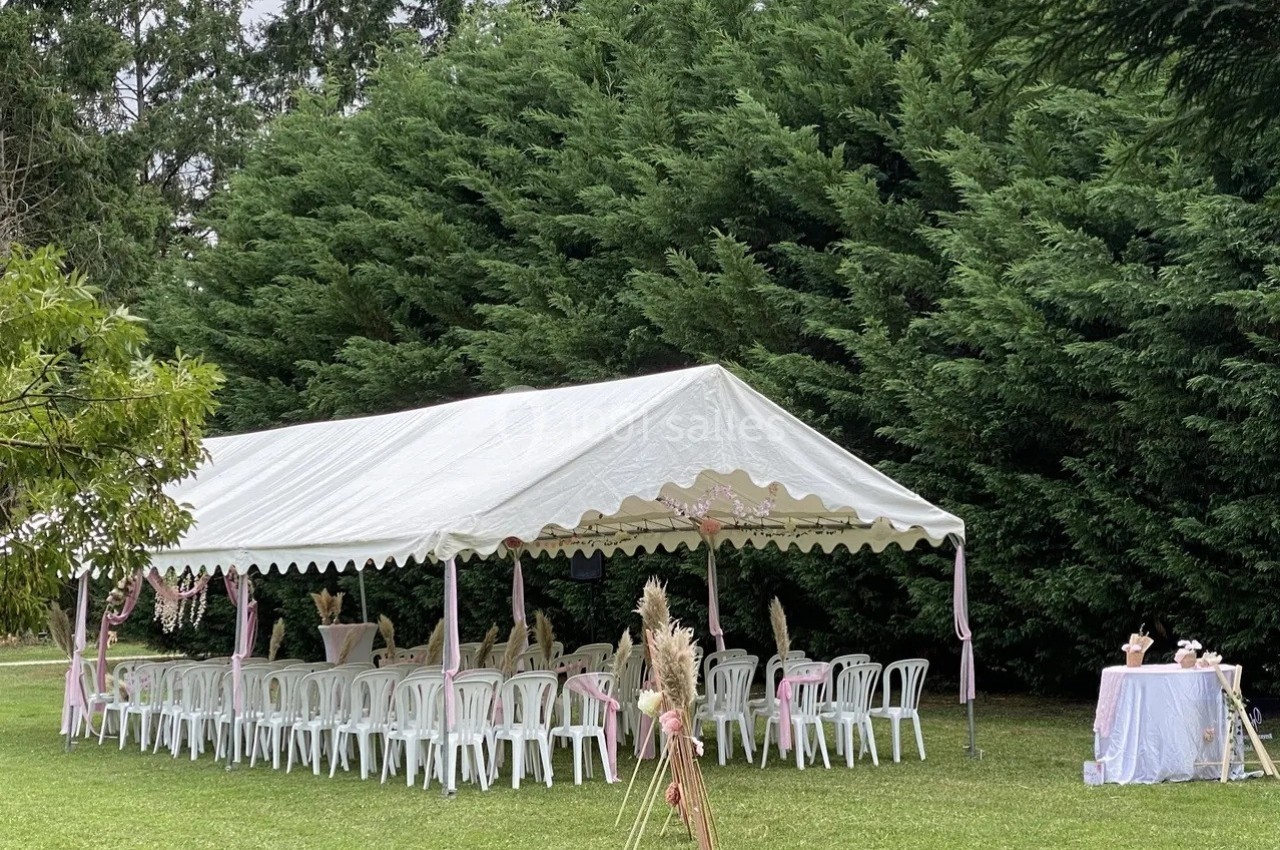 Tente blanche installée dans un jardin, entourée de chaises et décorée pour un événement en plein air.