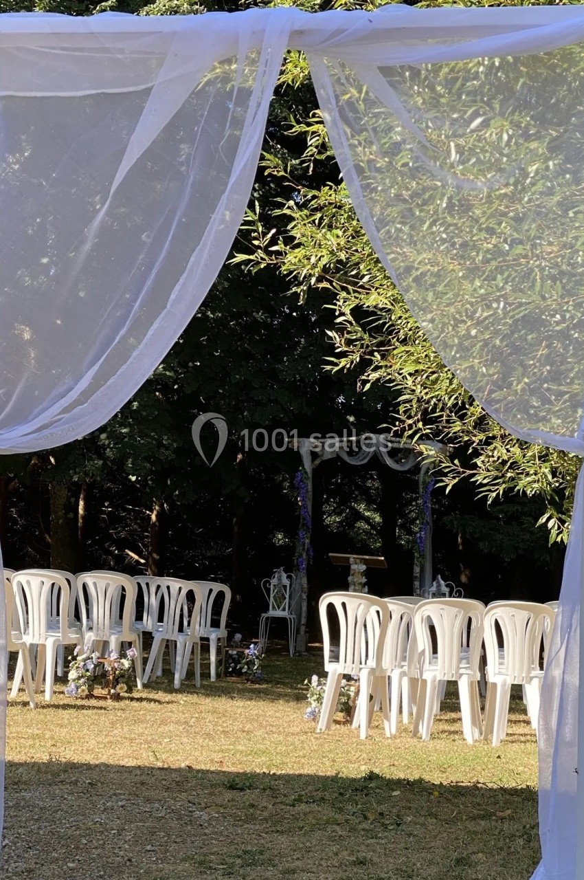 Chaises blanches disposées en extérieur sous un voile blanc, face à une arche décorée pour une cérémonie.