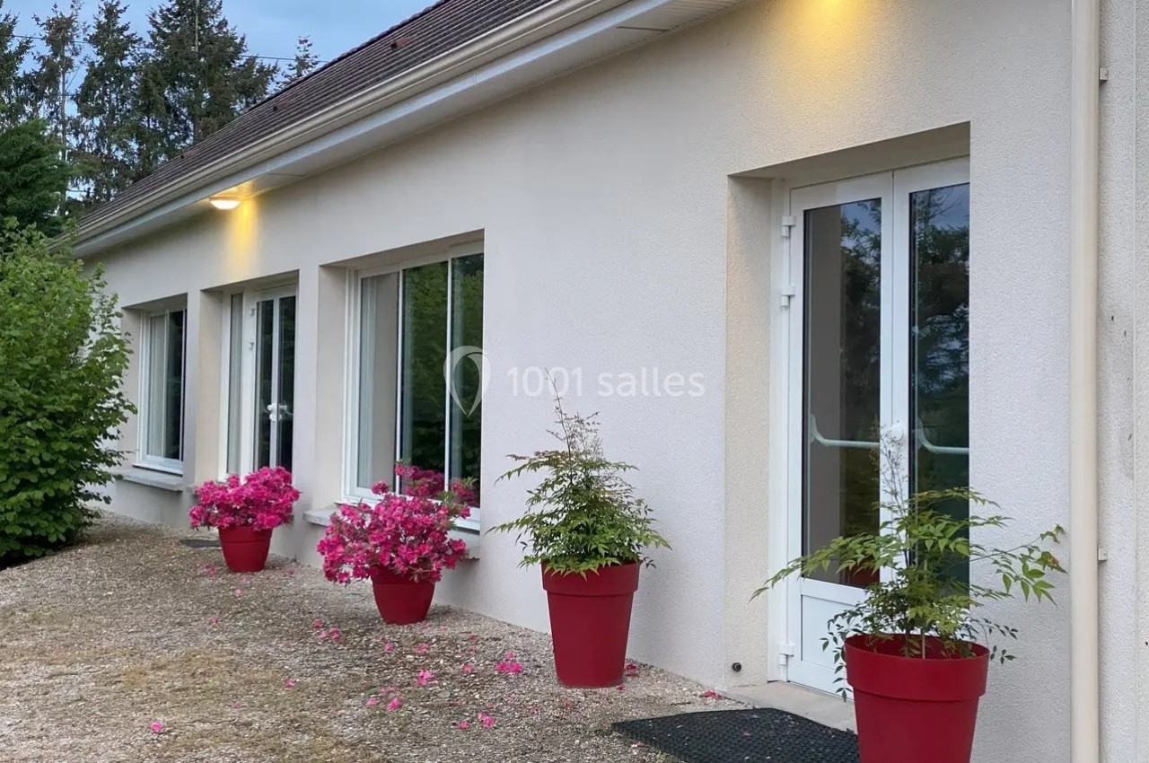 Façade d'une maison avec des fenêtres et des portes blanches, décorée de pots rouges contenant des plantes et des fleurs.