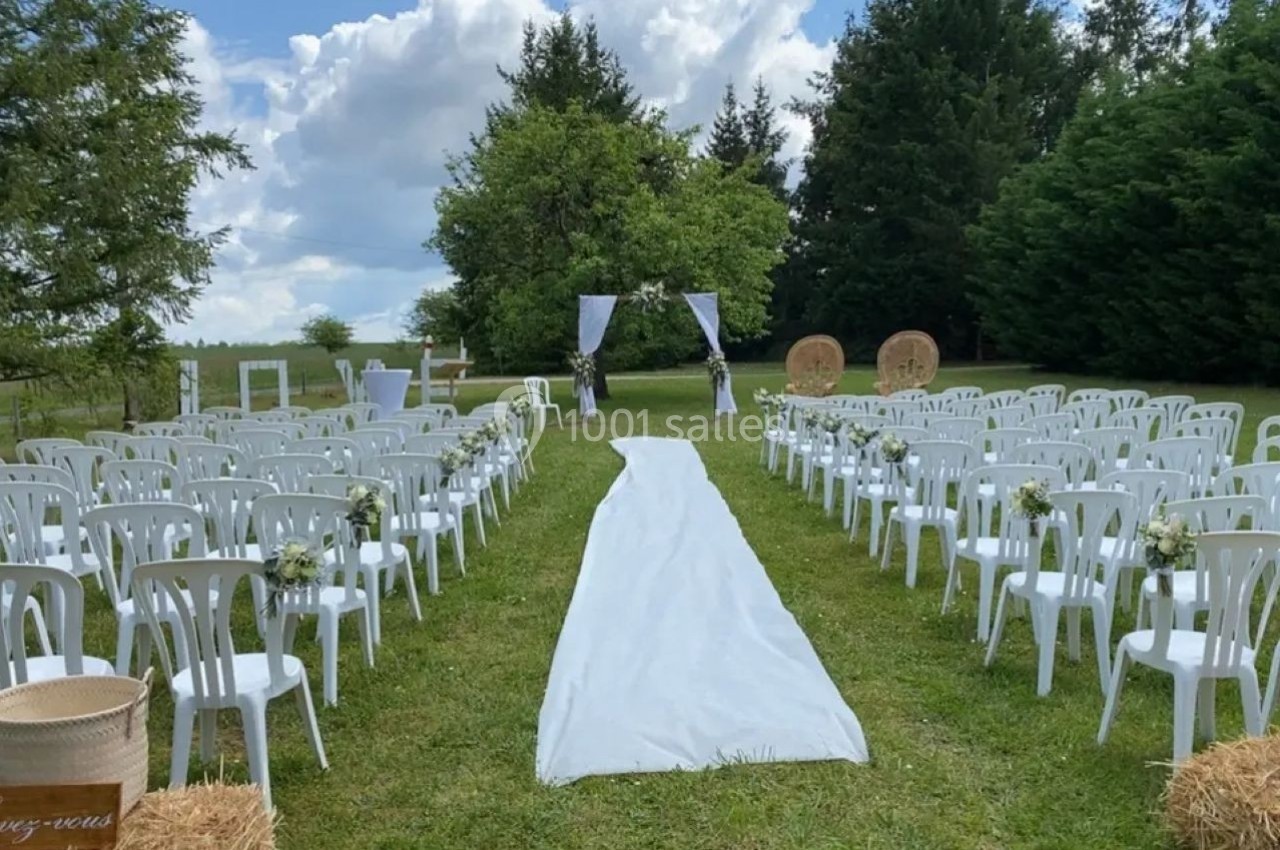 Allée centrale bordée de chaises blanches, menant à une arche décorée pour une cérémonie en plein air.