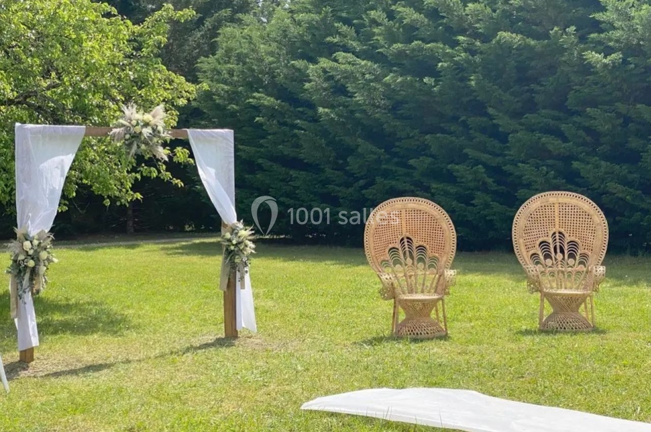 Arche décorée de fleurs et deux fauteuils en rotin sur une pelouse, entourés de verdure.