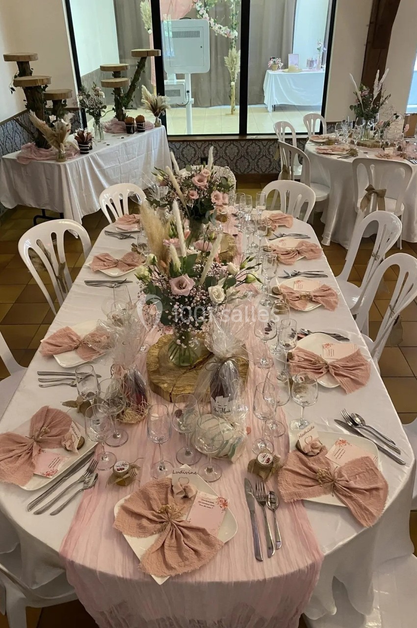 Table décorée pour un événement avec nappes blanches, serviettes roses pliées, fleurs et cadeaux d'invités.