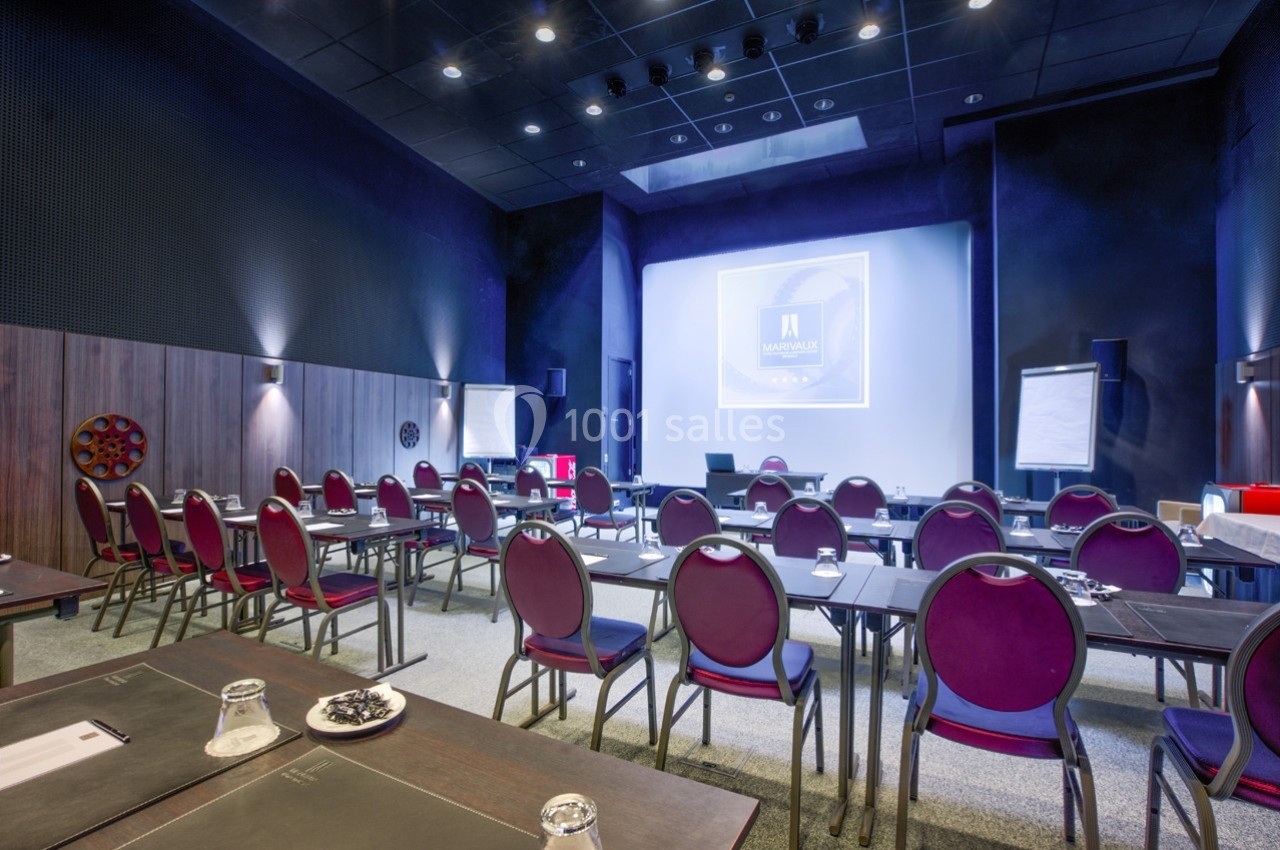 Salle de conférence équipée de tables, chaises, projecteur, écran et tableaux blancs dans un cadre moderne.