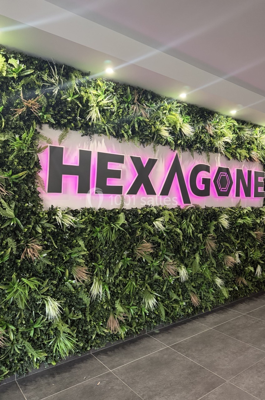 Mur végétal avec le logo ’HEXAGONE’ lumineux en rose, situé dans un espace intérieur moderne avec sol en carrelage.