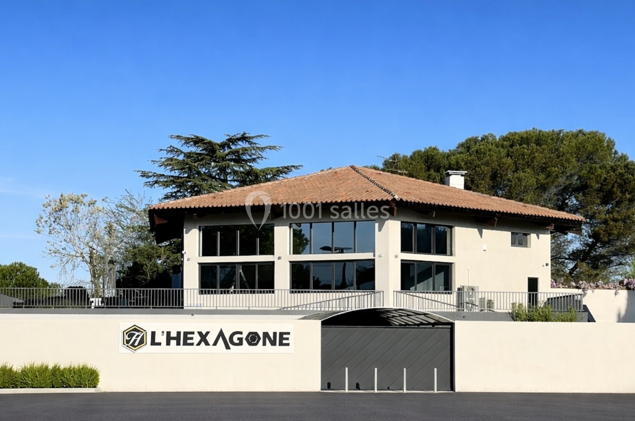 Bâtiment moderne à deux étages avec toit en tuiles, grandes baies vitrées et enseigne ’L'Hexagone’ sur un mur clair.