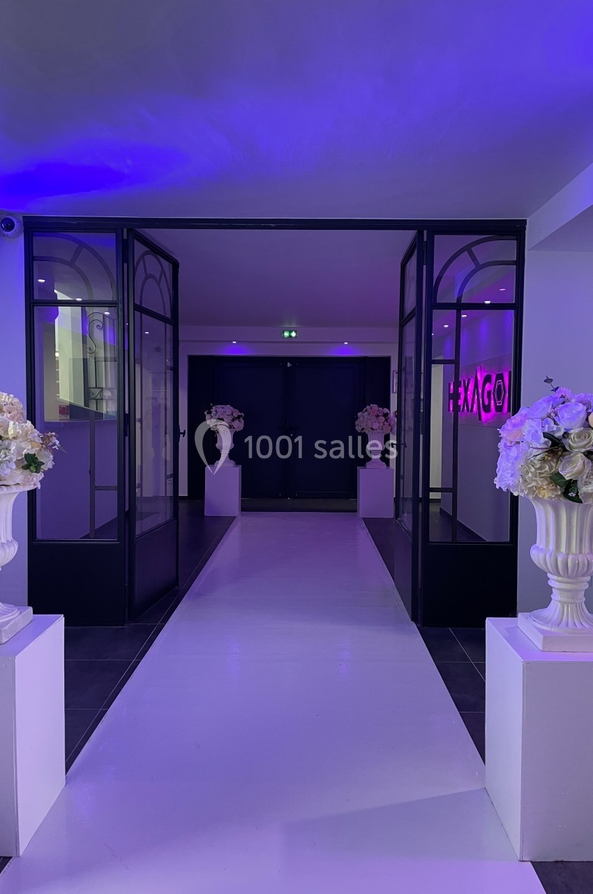 Entrée élégante avec double porte vitrée, décorée de colonnes blanches et bouquets de fleurs sous éclairage violet.