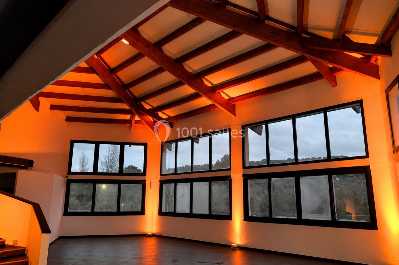 Grande pièce avec plafond en bois, baies vitrées offrant une vue sur l'extérieur et éclairage intérieur chaleureux.