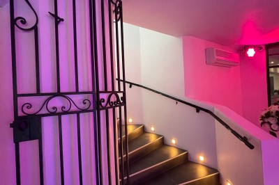 Escalier intérieur éclairé par des lumières au sol, avec une rampe et une porte en fer forgé décorative.